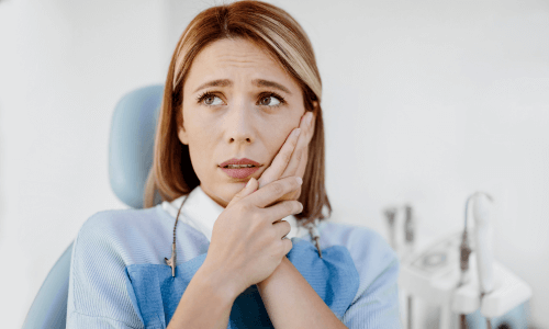 Woman sitting in a dental chair, holding her cheek in discomfort Woman sitting in a dental chair, holding her cheek in discomfort